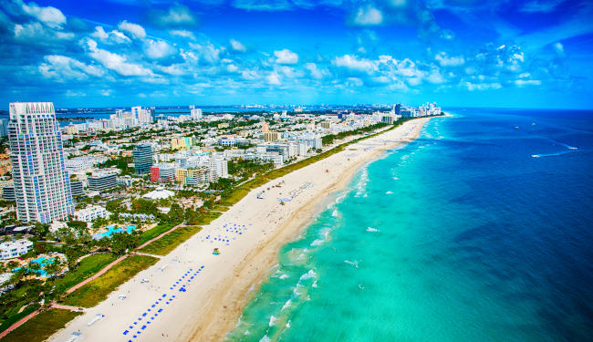 Aerial view of white sand beach with tall buildings overlooking the water.