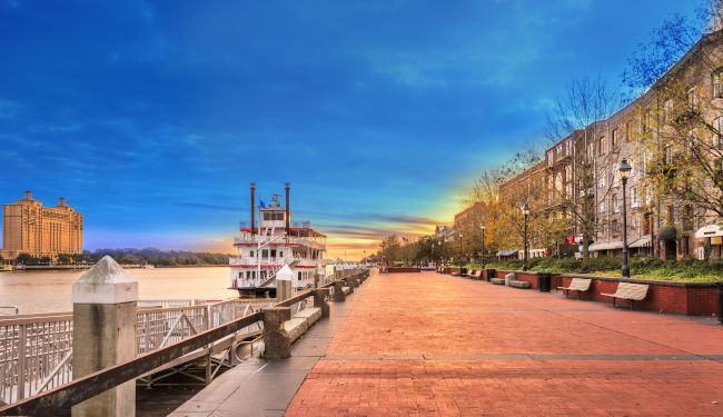 A historic steamboat in the river and brownstone homes overlooking the water.