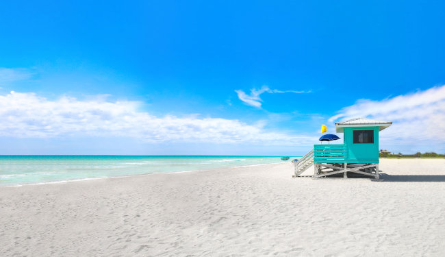 Colorful lifeguard shack on white sands beach overlooking the ocean on a sunny day.